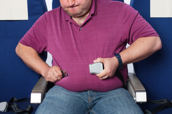 Passageiro obeso tenta apertar o cinto de segurança em poltrona de avião comercial