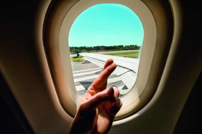 Pessoa cruzando os dedos em frente a janela de um avião prestes a decolar