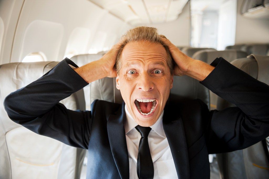 Homem apavorado grita dentro de avião com as mãos na cabeça