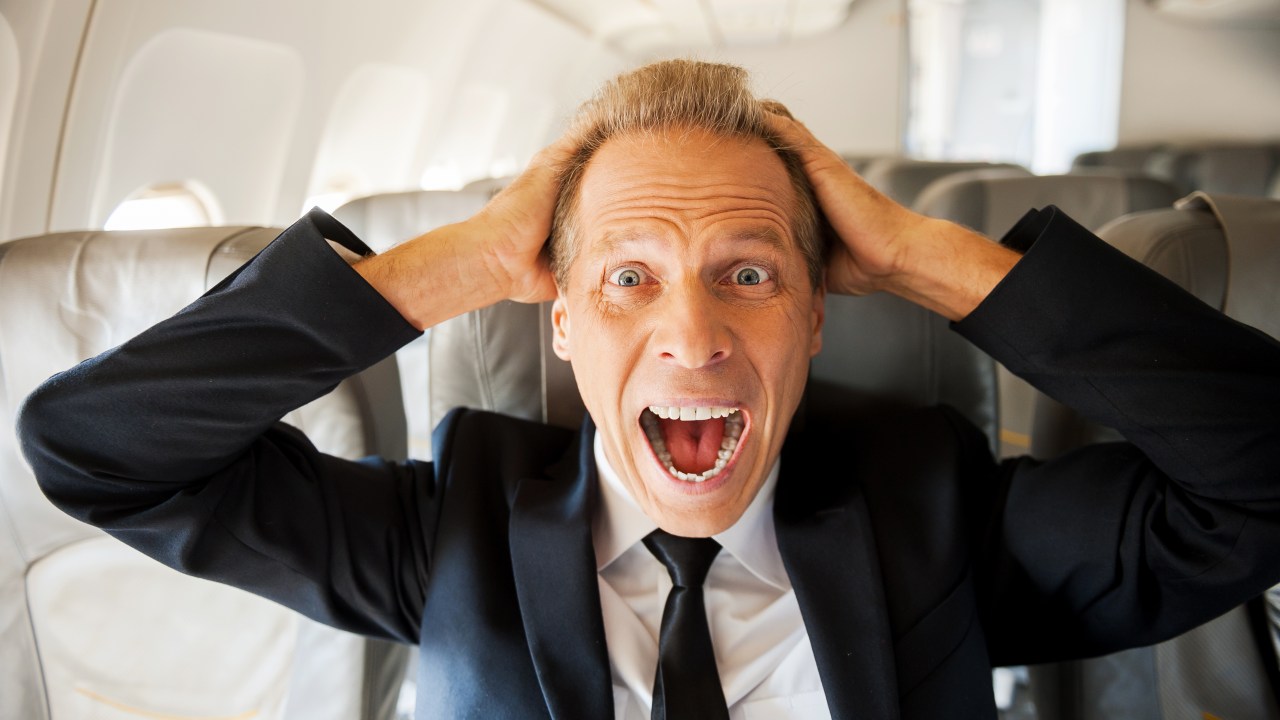 Homem apavorado grita dentro de avião com as mãos na cabeça