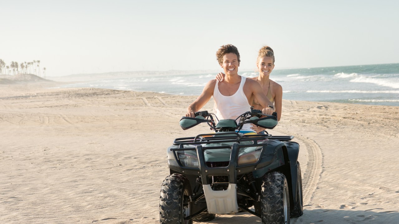 Casal dirigindo um Quad ATV na praia