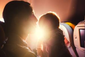 Mãe e bebê sentados em poltrona de avião durante voo comercial com sol ao fundo
