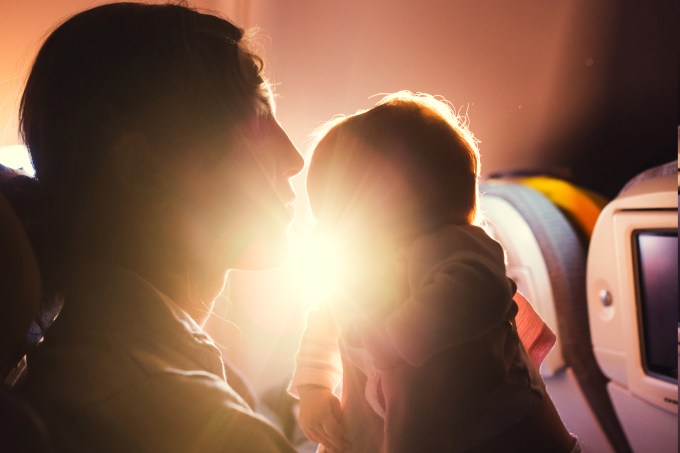 Mãe e bebê sentados em poltrona de avião durante voo comercial com sol ao fundo