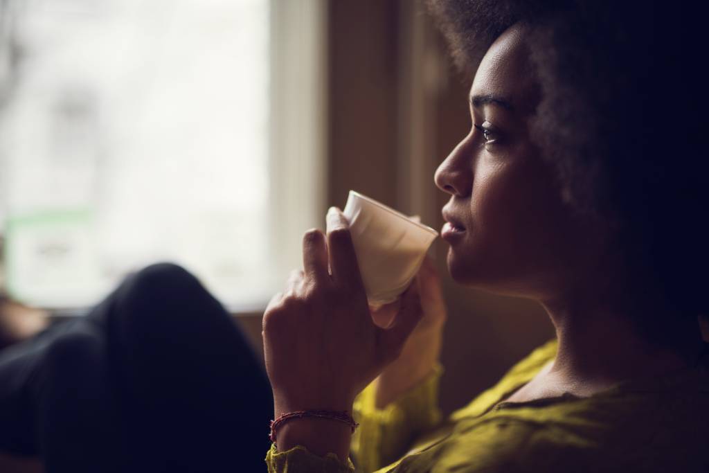 Mulher tomando café dentro de casa em um dia frio de inverno com feição de tristeza