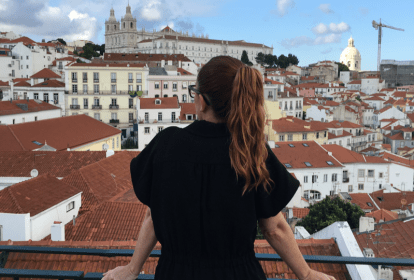 A imagem mostra uma mulher de costas. Ela está olhando para Lisboa