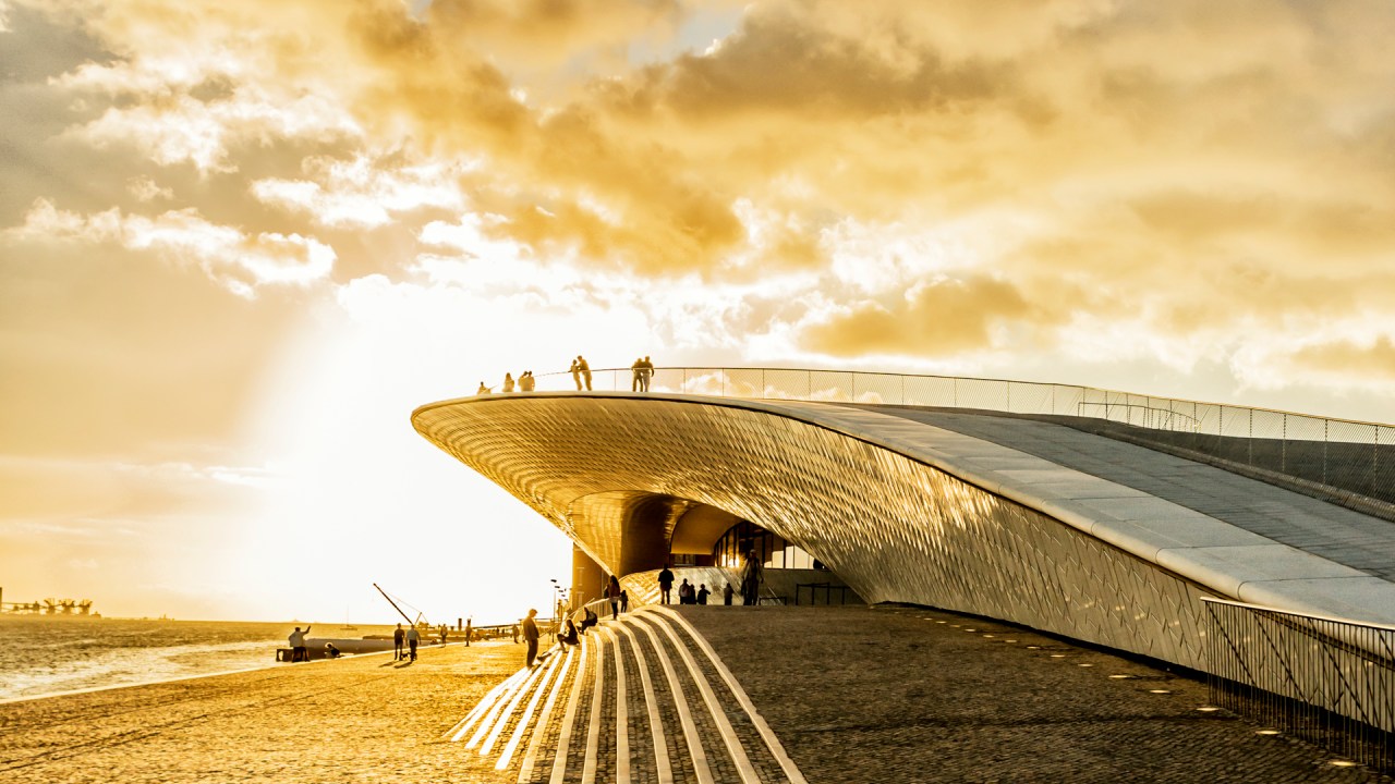 Museu de ares futuristas com linhas arredondadas e uma escadaria em primeiro plano, à beira-rio e ao pôr do sol