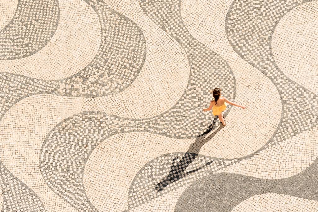 Menina de vestido amarelo anda de braços abertos sobre calçada portuguesa