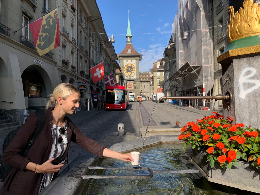 Água direto da fonte na Kramgasse, uma das ruas mais emblemáticas de Berna, com a Torre do Relógio ao fundo.