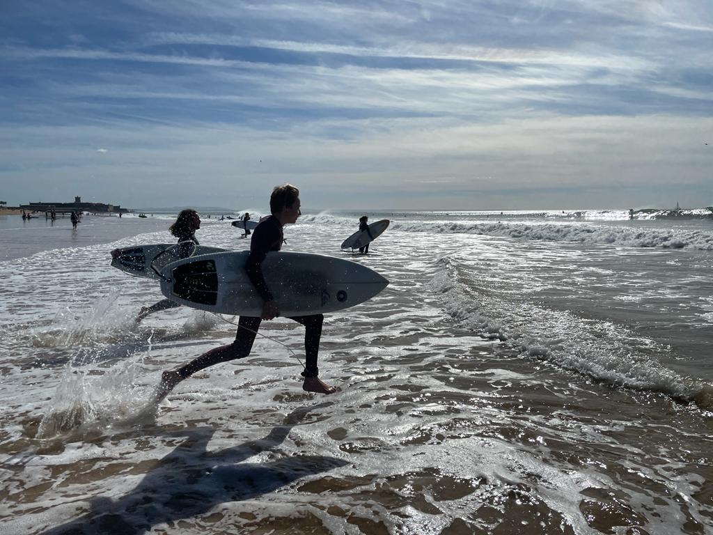 Três jovens entram correndo no mar segurando pranchas de surfe
