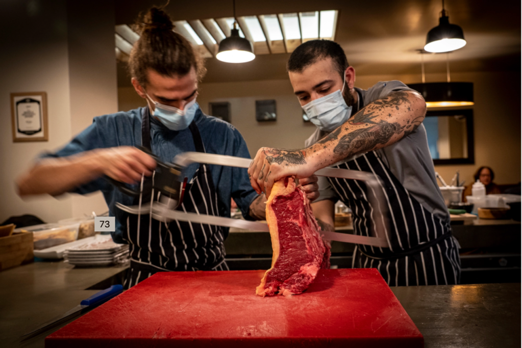 Dois homens serram um grande pedaço de carne crua com um serrote no balcão de um restaurante na Ilha da Madeira, em Portugal