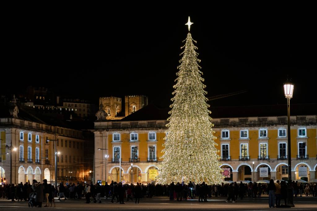 Prédio amarelo com uma grande árvore de Natal na frente, coberta de luzes amarelas e coroada com uma estrela