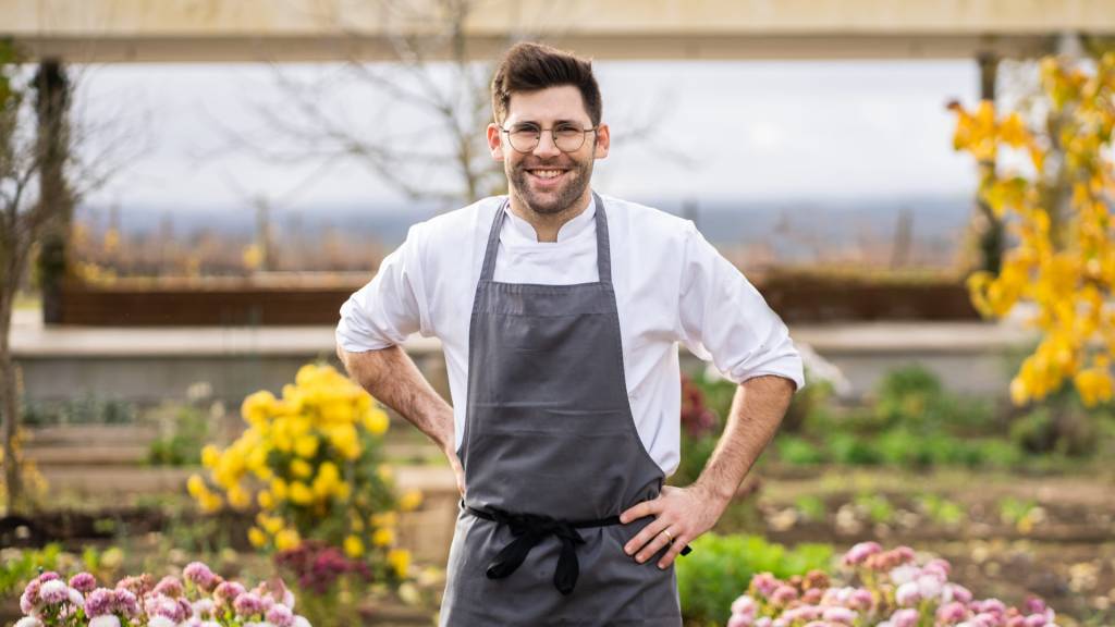 Chef do restaurante Esporão com a mão na cintura, camisa branca e avental cinza, no jardim da herdade