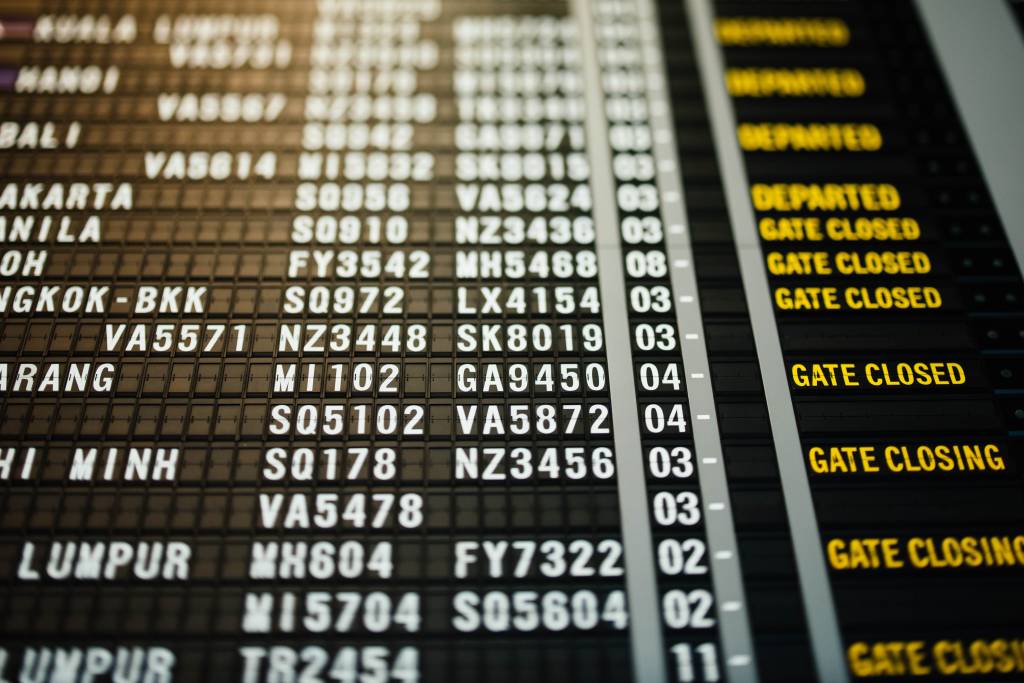 Painel preto com letras brancas e amarelas anunciando os voos em um aeroporto internacional
