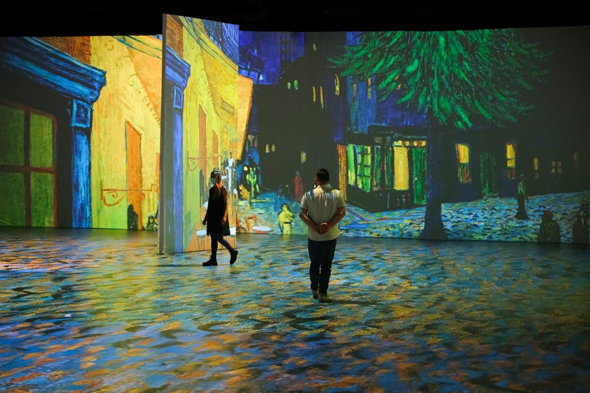 Na imagem, vemos pessoas andando entre espaços onde as pinturas de Van Gogh estão sendo projetadas.
