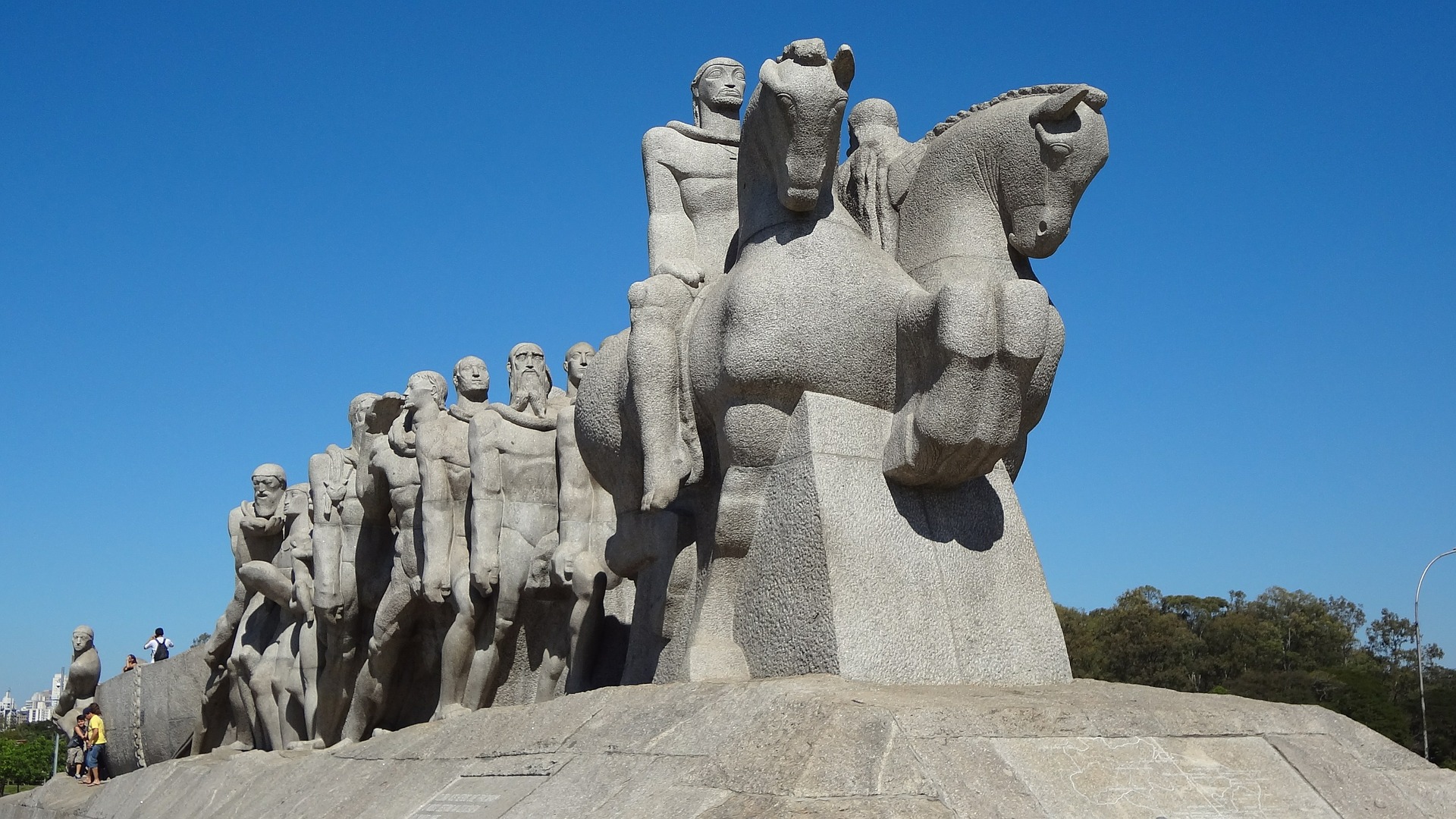 Na imagem, vemos uma foto do Monumento às Bandeiras, uma enorme esculturas com vários homens montados em cavalos.