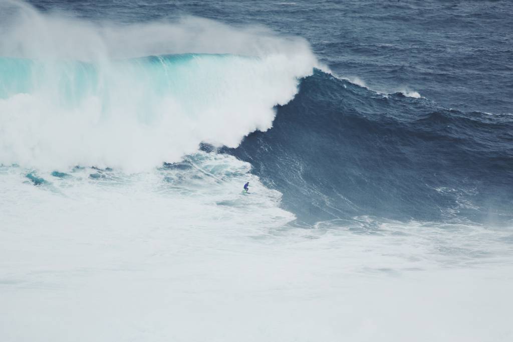 Um homem surfando uma onda gigante a quebrar sobre ele ,a Nazaré, em Portugal