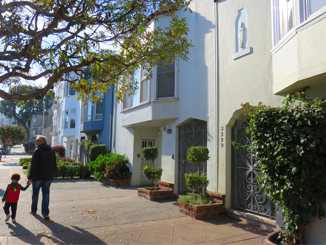 Pai e filho andando numa calçada em São Francisco. Do lado direito casas típicas da cidade