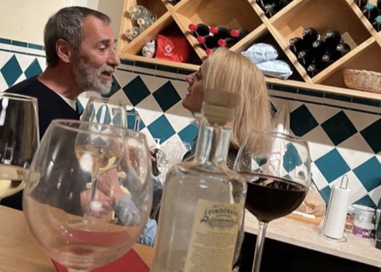 Um homem e uma mulher conversando, com copos de vinho e uma garrafa em primeiro plano