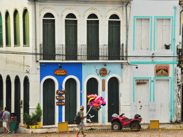 Casario colonial ao fundo com homem carregando balões coloridos.