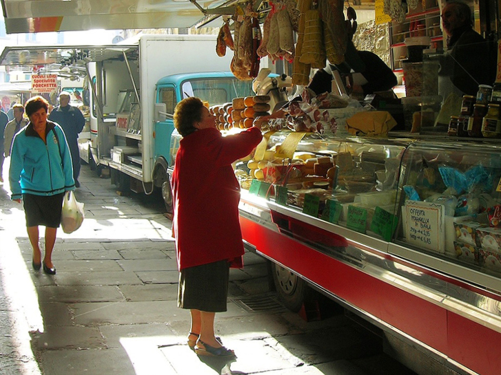 Uma senhora comprando frios e laticínios numa banca típica da Toscana