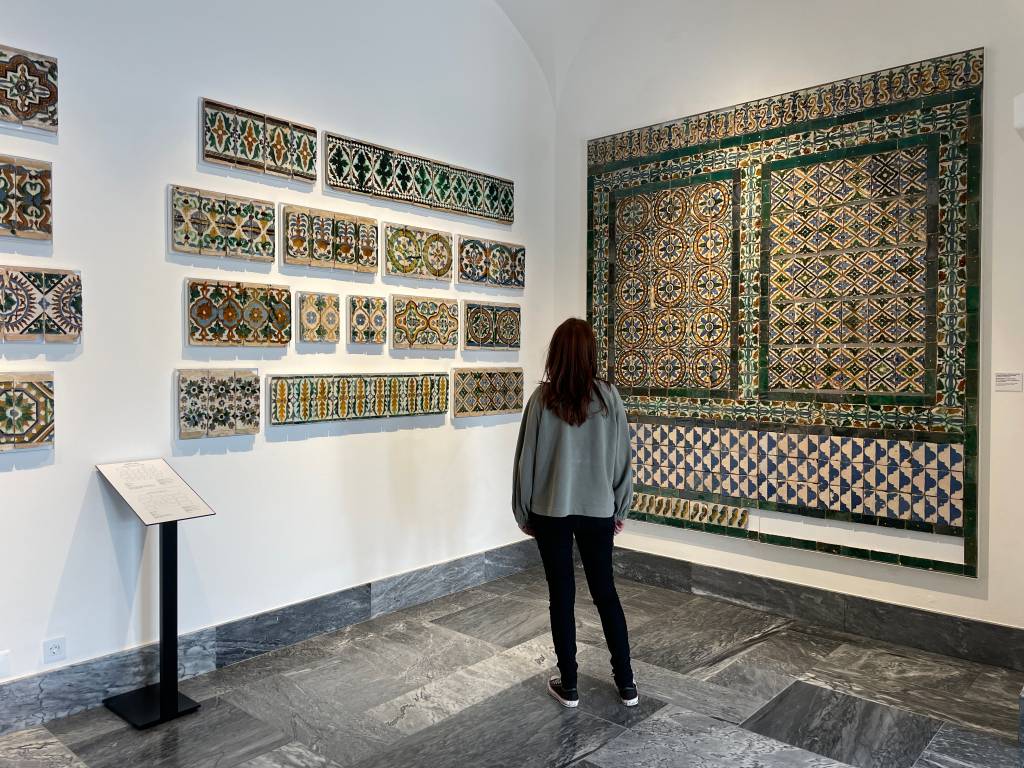 Mulher em frente a coleções de antigos azulejos na parede de um museu