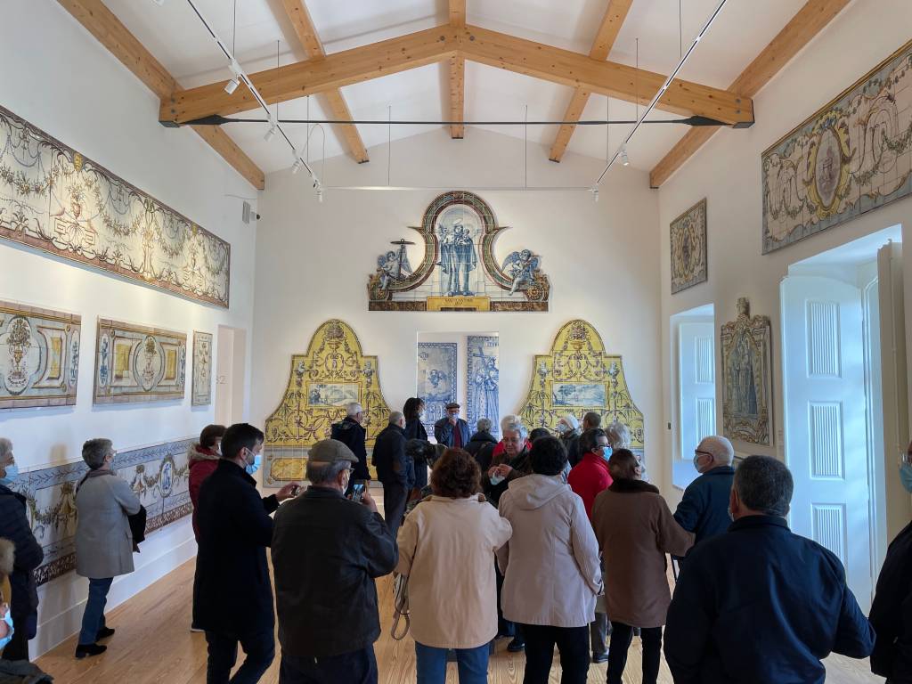 Um grupo de pessoas observa alguns painéis de azulejo nas paredes de um museu