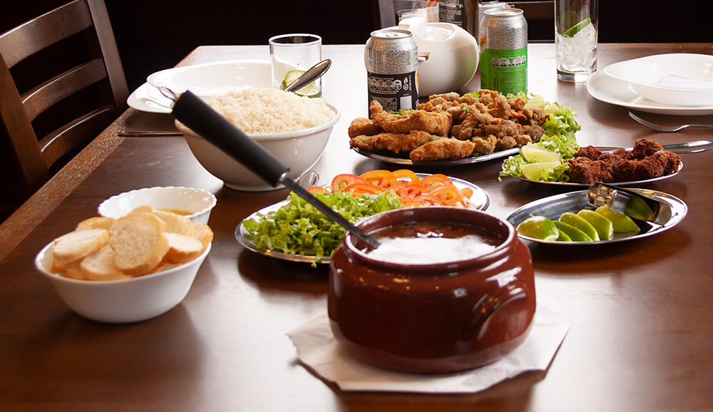 A fotografia colorida mostra uma mesa servida com salada, frutos do mar e uma panela de barro com carne e caldo