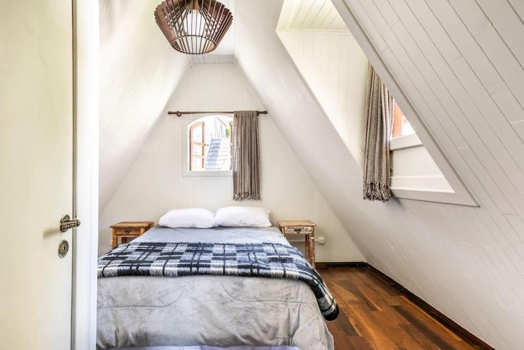 A imagem colorida mostra um quarto com telhado inclinado onde há uma cama de casal