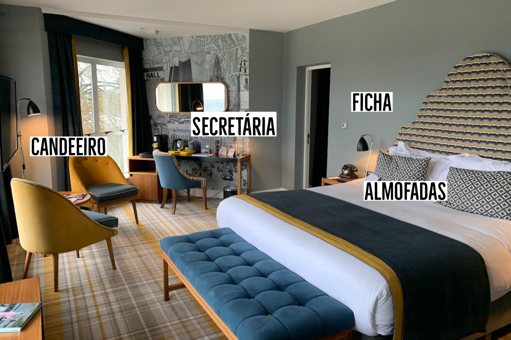 Um quarto com cama de casal, escrivaninha e duas poltronas, em tons de azul e bege