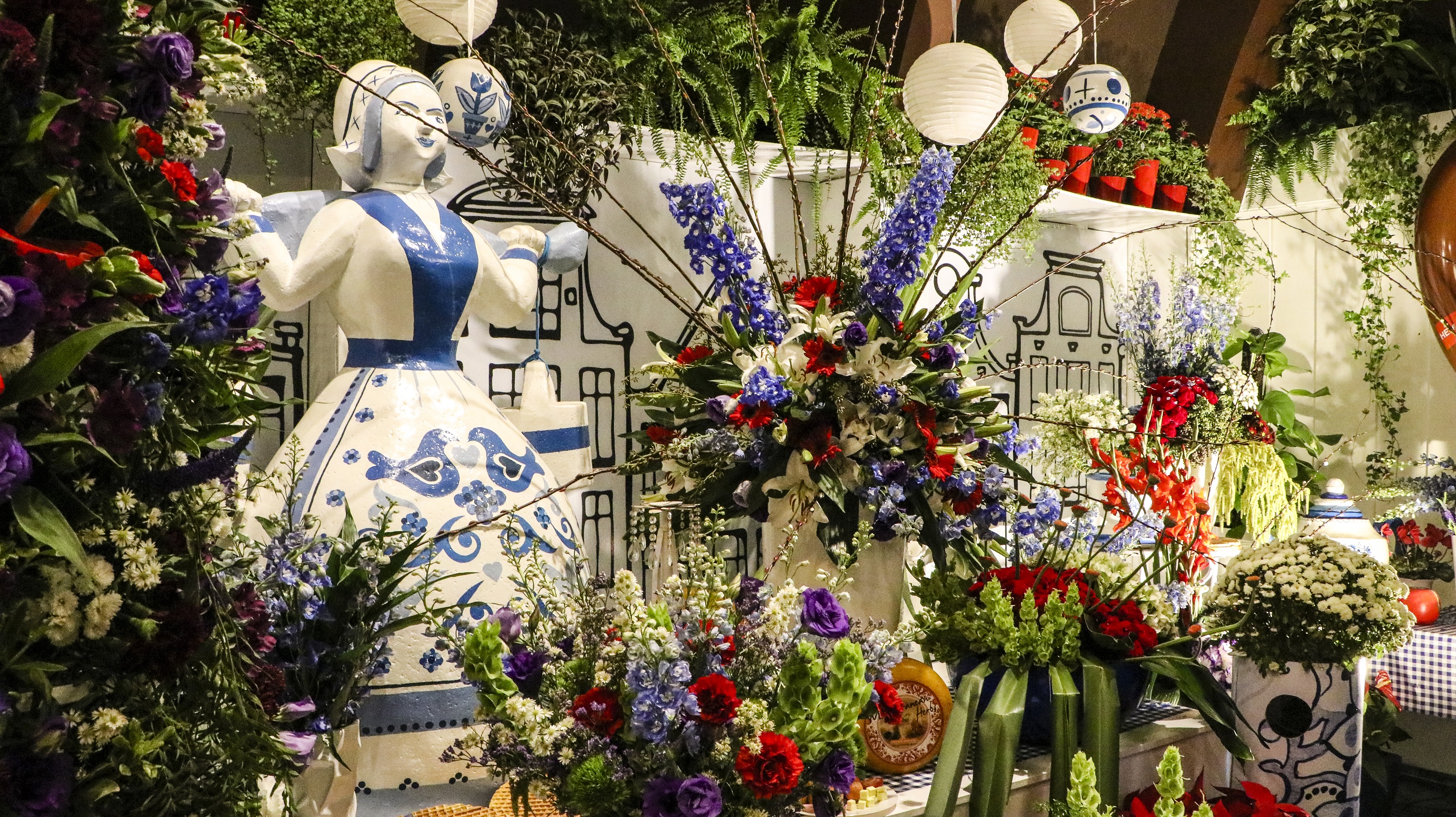A fotografia colorida mostra vários arranjos de flores e bonecos de porcelana brancos com orgamentos azuis.