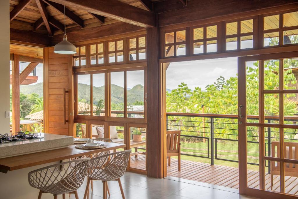 Casas Gengibre, Alto Paraíso de Goiás, Goiás A fotografia colorida mostra o interior de uma casas e a vista da sua varanda de dentro da casa. Os móveis e a decoração são de madeira, bem como o batente das portas e janelas. Da varanda vê-se copas de árvores verde claro e montanhas verde escuras ao fundo.