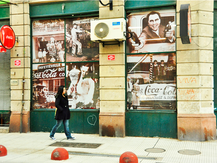 Mulher passa em frente a um mural com temas vintage da Coca-Cola.