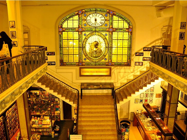 Visão superior da livraria Más Puro Verso com a escada de mármore e vitrais centralizados.