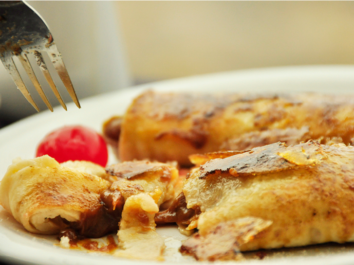 Prato com crepe recheado recém cortado, com uma cereja e garfo.