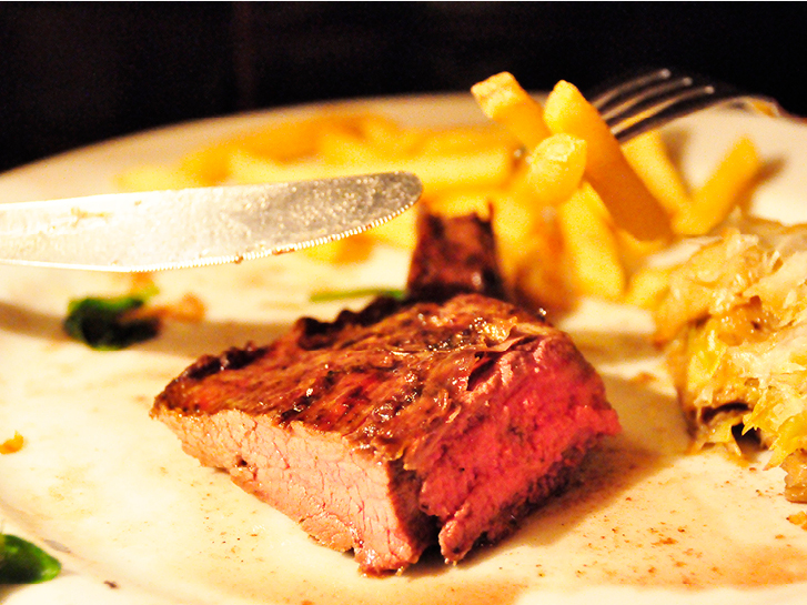 Carne mal passada em primeiro plano com batatas fritas ao fundo