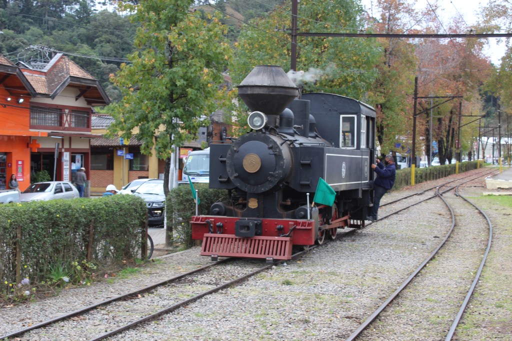 A imagem mostra um trem preto e vermelho soltando fumaça