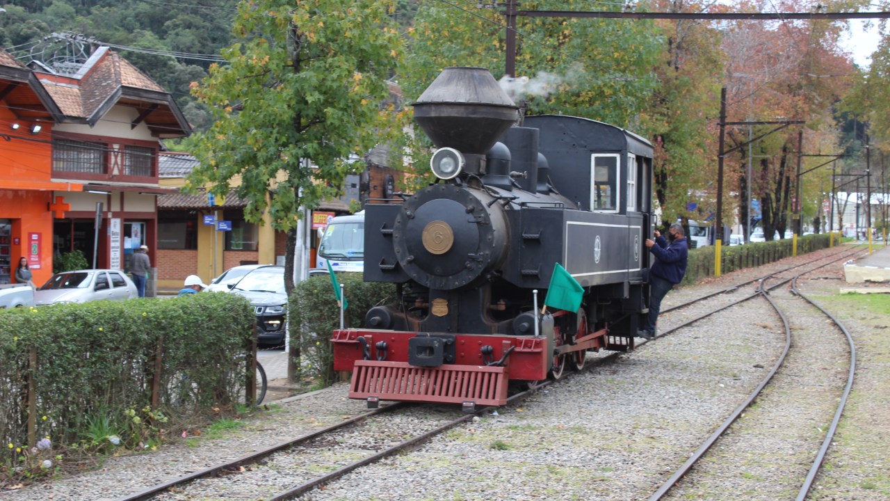 A imagem mostra um trem preto e vermelho soltando fumaça
