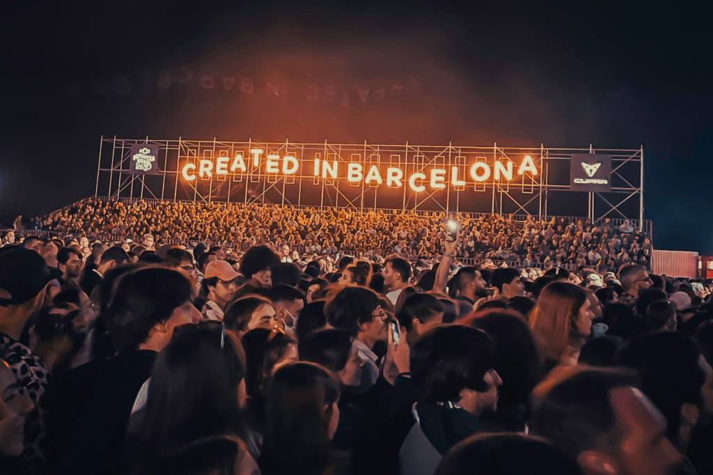 Multidão em um festival de música, com um letreiro dizendo created in Barcelona ao fundo