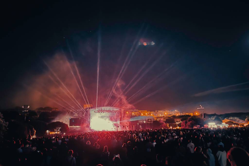 Multidão em frente a um palco em um show, com luzes vermelhas