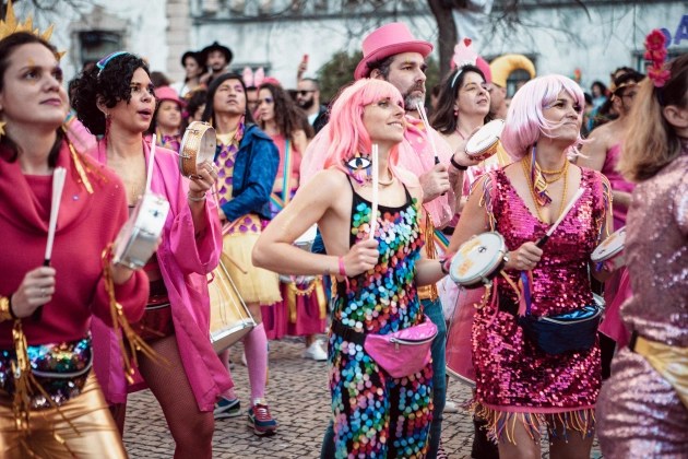 Mulheres de peruca cor de rosa, homens de chapéu e pessoas fantasiadas tocam num bloco de carnaval em Lisboa