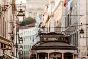 Prédios de fachadas em tons pastel com luminárias e um pedaço de um bonde elétrico com uma placa que diz M Moniz