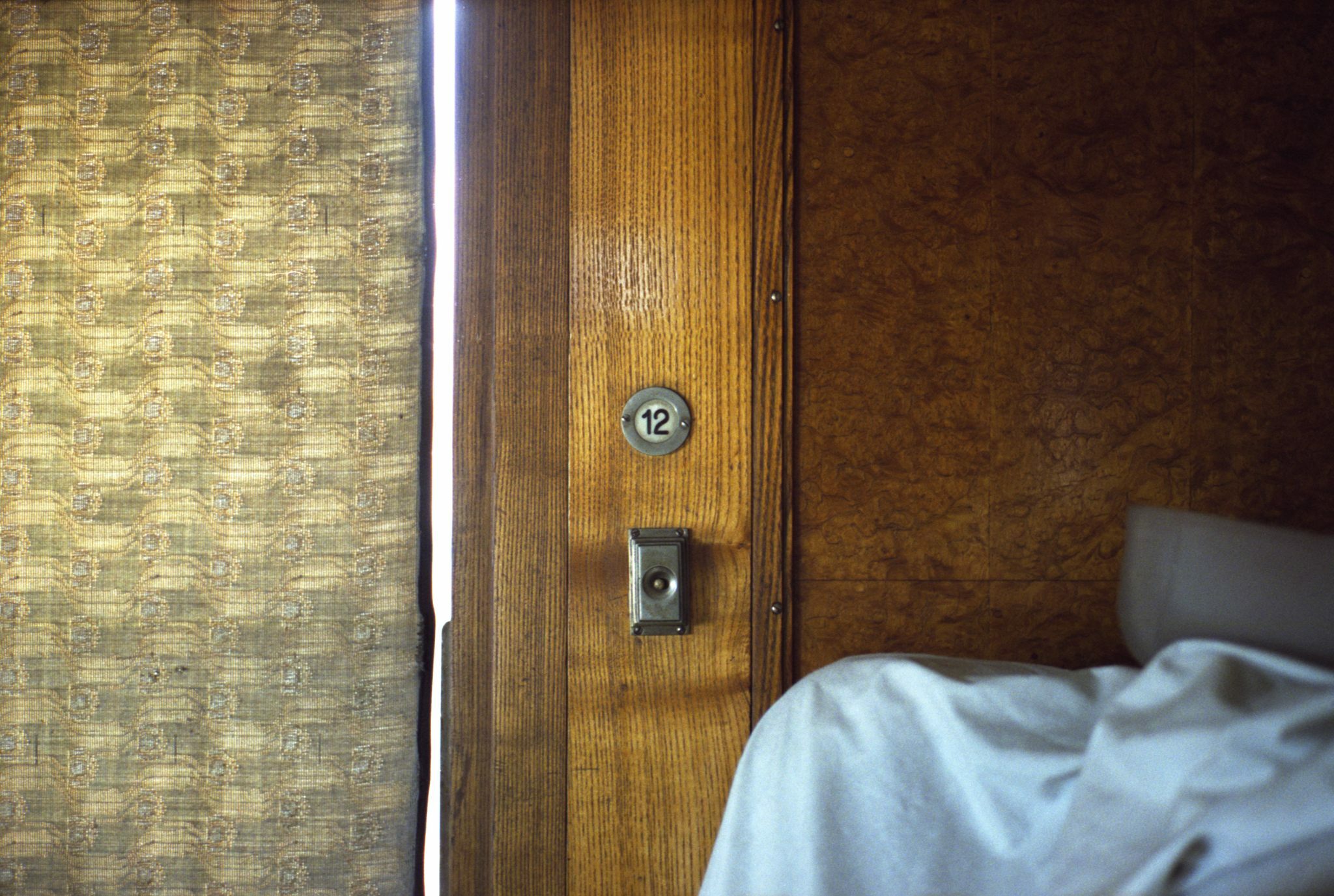A imagem mostra uma parede e a porta de um quarto em um vagão de trem antigo
