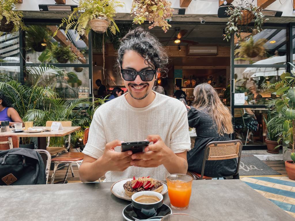 Nouã fotografando com o celular o seu brunch com café, suco de laranja e panquecas de chocolate