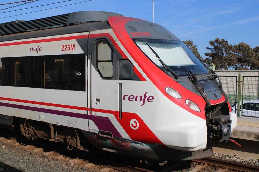 A imagem colorida mostra um trem moderno branco e vermelho, com o logo da empresa Renfe