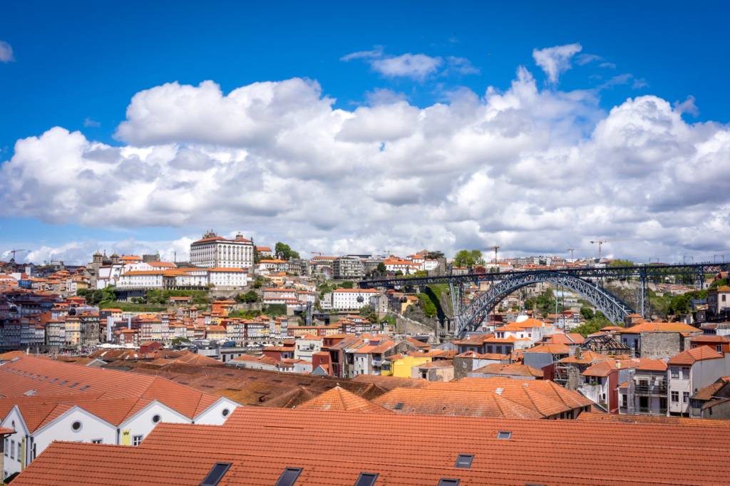 Telhadas em primeiro plano e, ao fundo, a Ponte D. Luís I e as casinhas coloridas da cidade do Porto