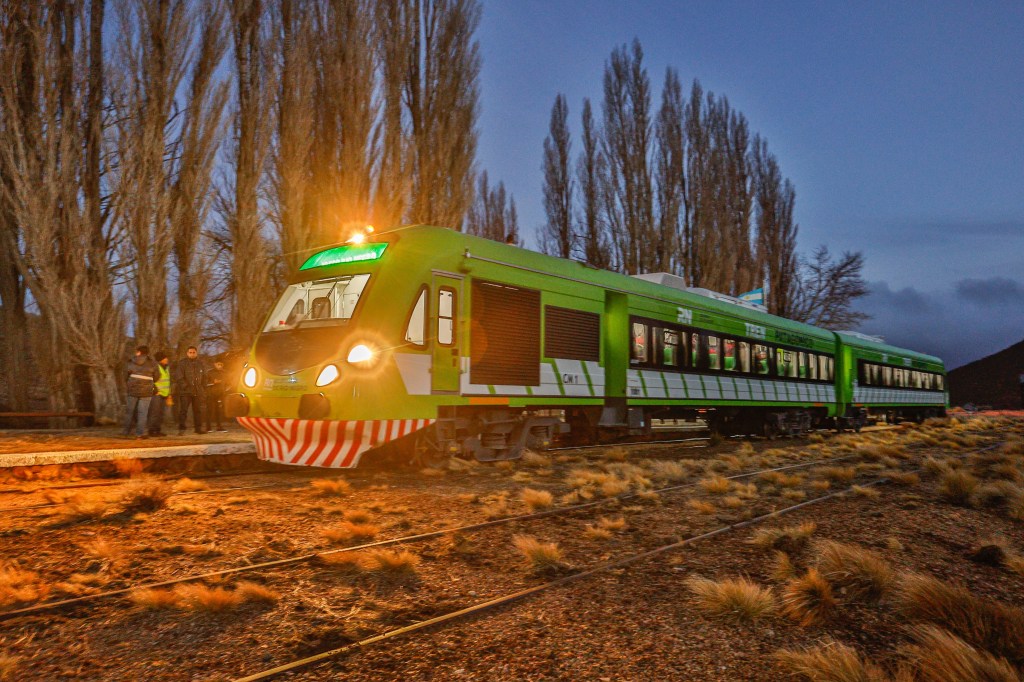 A imagem mostra um trem verde fazendo um trajeto noturno