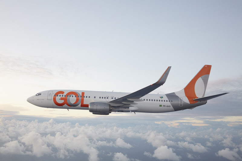 A imagem mostra um avião com detalhes brancos e laranjas e o nome da marca Gol