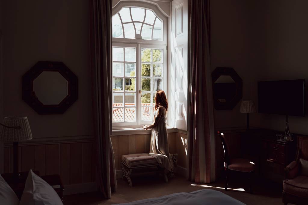 Mulher de costas na janela de um quarto de hotel, em conta-luz