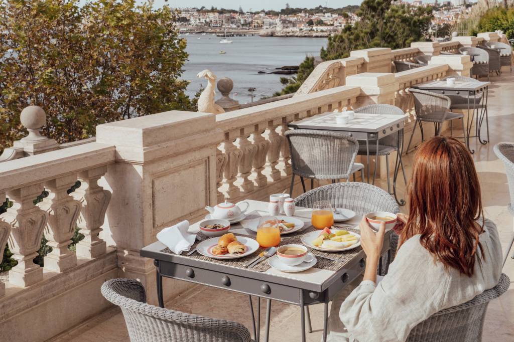 Mesa de café da manhã com vista do mar e uma mulher sentada de costas