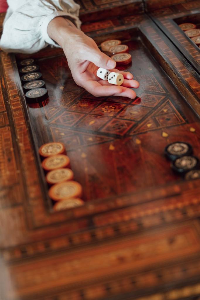 Detalhes de uma mão segurando dois dados sobre uma mesa de jogos em madeira